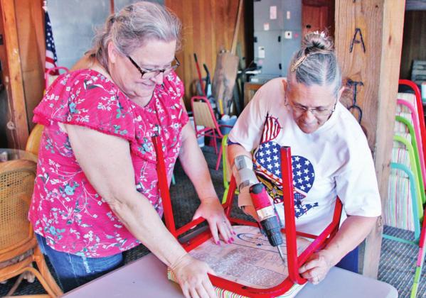 Volunteers Juliana Jordan, left, of Freestone County, and Peggy Grove, of Wortham, work together to re-attach the bottoms of chairs to their frames. The project is part of the new building for Veterans Partners of Texas. Photo by Roxanne Thompson/The Mexia News